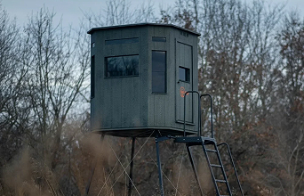 A hunting blind on stilts surrounded by trees and shrubs.